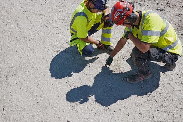 Two construction workers sketch in the sand